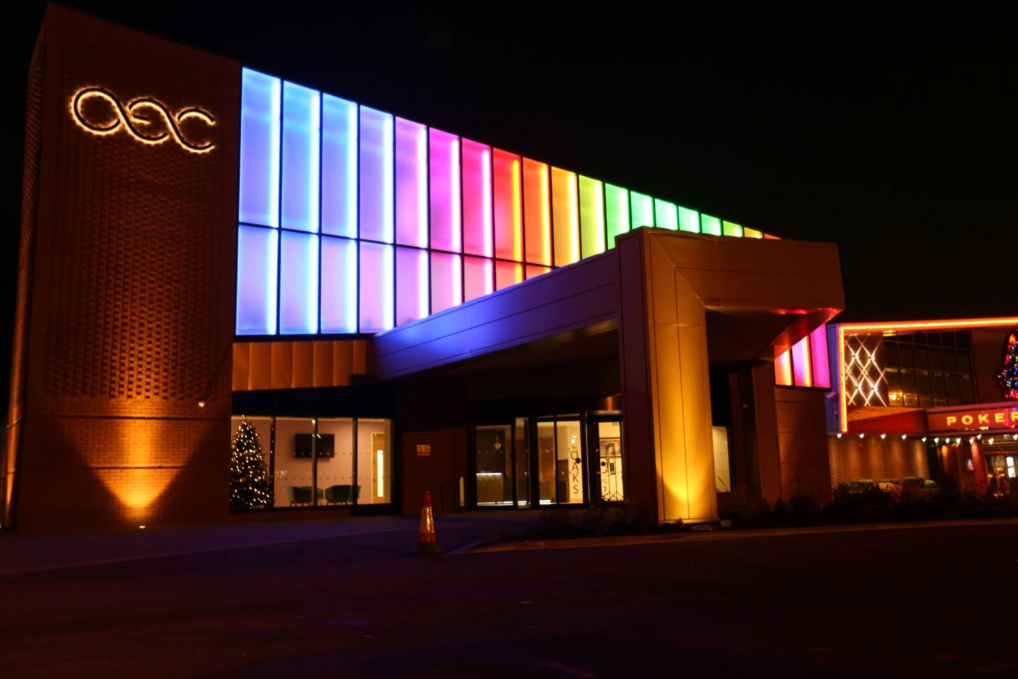 Urban bridge lit with vibrant pink neon lights, reflecting on the river, with illuminated skyscrapers in the background.