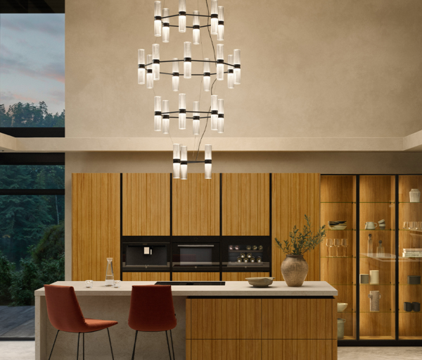 Cuisine moderne avec un grand lustre composé de multiples cylindres en verre diffusant. une lumière chaude au-dessus d’un îlot central en pierre et bois