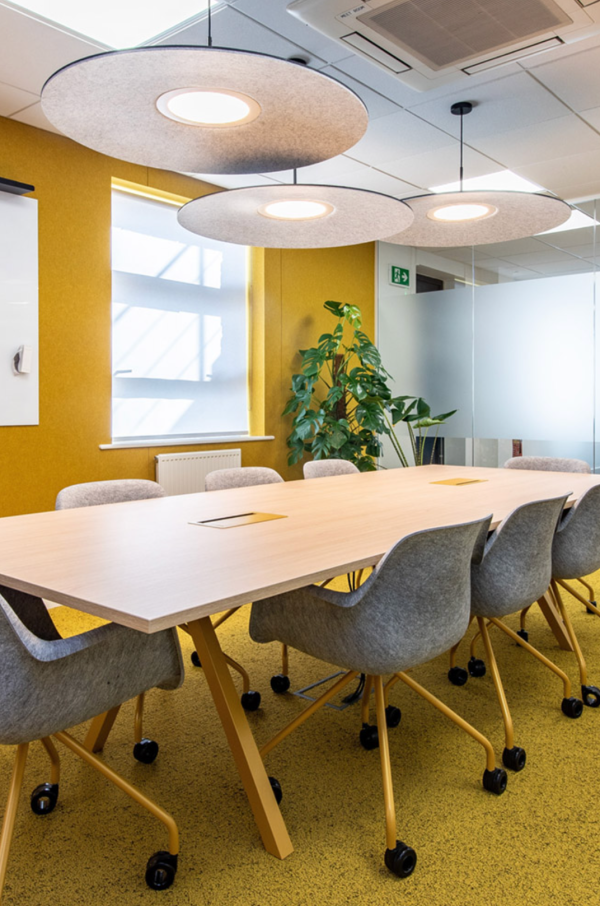 Cone acoustic pendant lights by Luménear with a sleek circular design, casting a soft glow above a large meeting table in a warm, contemporary space.