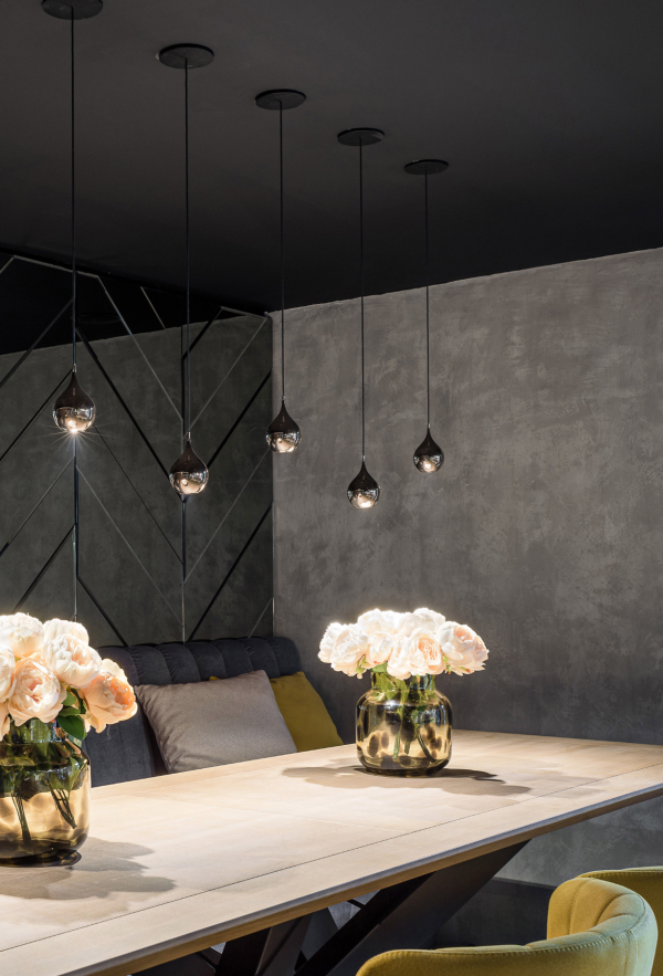 Espace moderne avec suspensions en forme de goutte diffusant une lumière douce au-dessus d’une table décorée de vases de fleurs, sur fond de mur en béton brut.