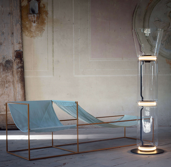Espace intérieur au style minimaliste avec fauteuils en tissu suspendu et lampe de sol design en verre transparent et anneaux lumineux LED.