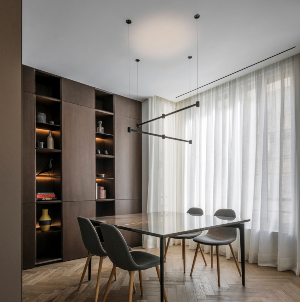 Salle à manger contemporaine avec suspension minimaliste noire au plafond et étagères intégrées rétroéclairées diffusant une lumière chaude.