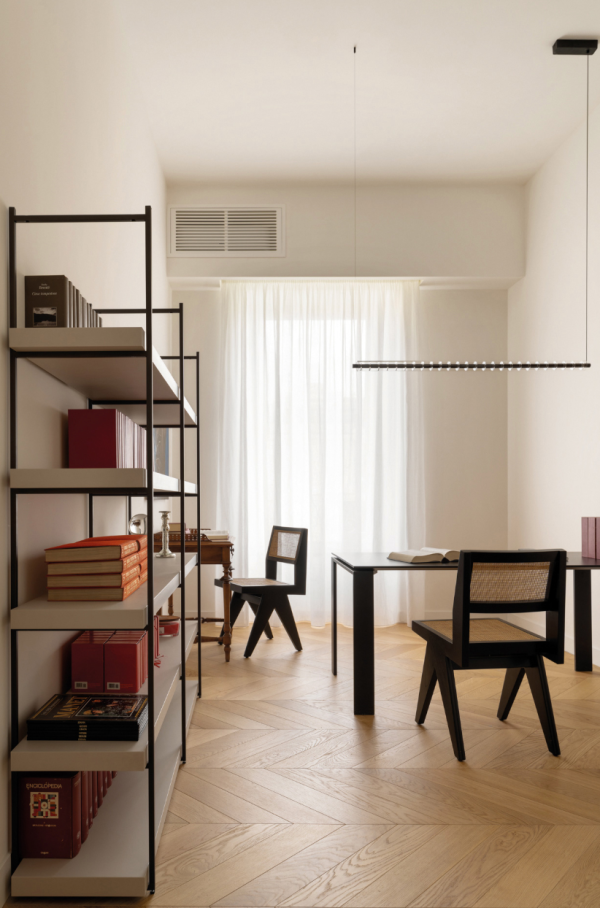 Bureau minimaliste avec suspension linéaire LED au-dessus d’un bureau noir, étagères garnies de livres et chaises en bois avec assise en cannage.