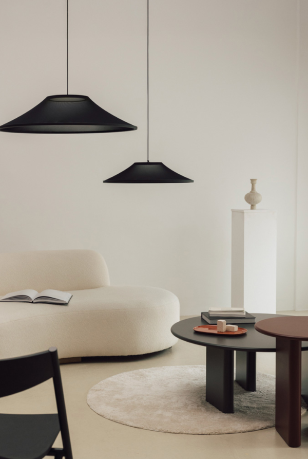 Séjour minimaliste avec deux suspensions noires en forme de large coupole diffusant une lumière douce au-dessus d’un canapé clair, pour une ambiance contemporaine.