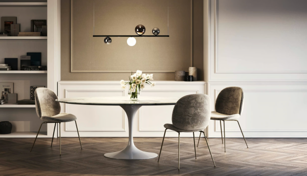Salle à manger élégante avec table ronde en marbre et chaises en velours, éclairée par une suspension moderne composée de sphères lumineuses et métalliques.