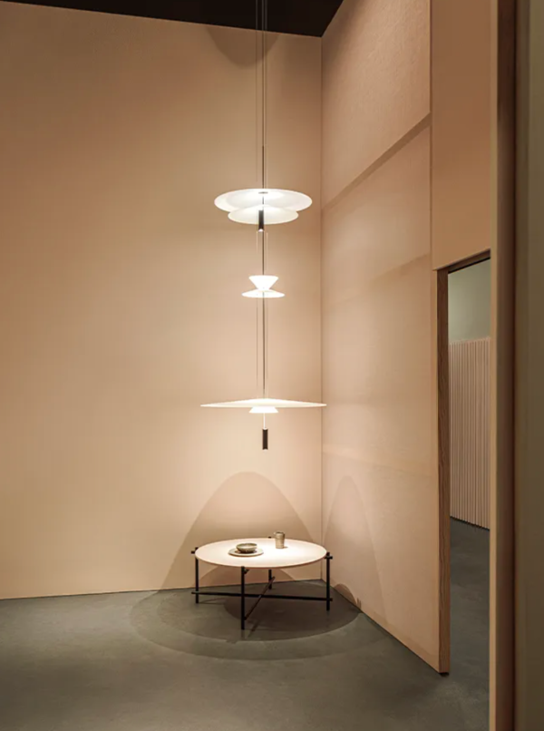Suspension design à plusieurs niveaux diffusant une lumière douce au-dessus d’une petite table ronde, créant une ambiance chaleureuse dans un espace minimaliste.