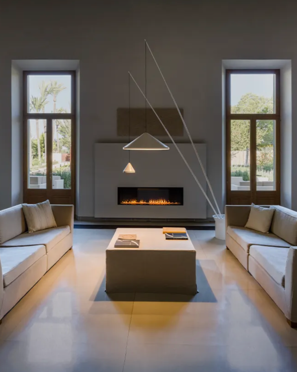 Séjour contemporain avec suspensions géométriques diffusant une lumière douce au-dessus d’une table basse, encadrée par deux canapés clairs et une cheminée moderne.