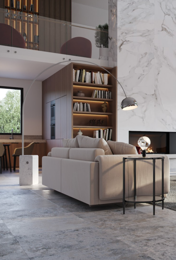 Salon moderne avec canapé beige, éclairé par un grand lampadaire arqué métallique, une lampe de table design et l’éclairage intégré d’une bibliothèque.
