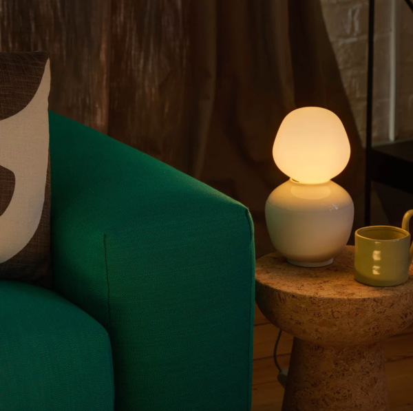 Petit coin cosy avec un canapé vert, une table d’appoint en liège et une lampe de table en verre diffusant une lumière chaude.