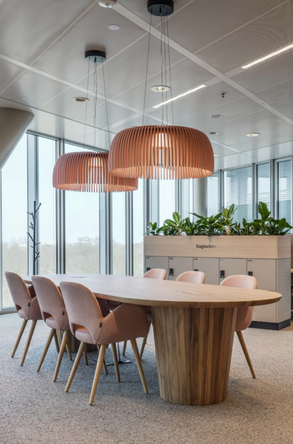 Breeze wooden openwork pendant lights by Luménear, casting a warm glow above a solid wood meeting table in a bright, plant-filled space.