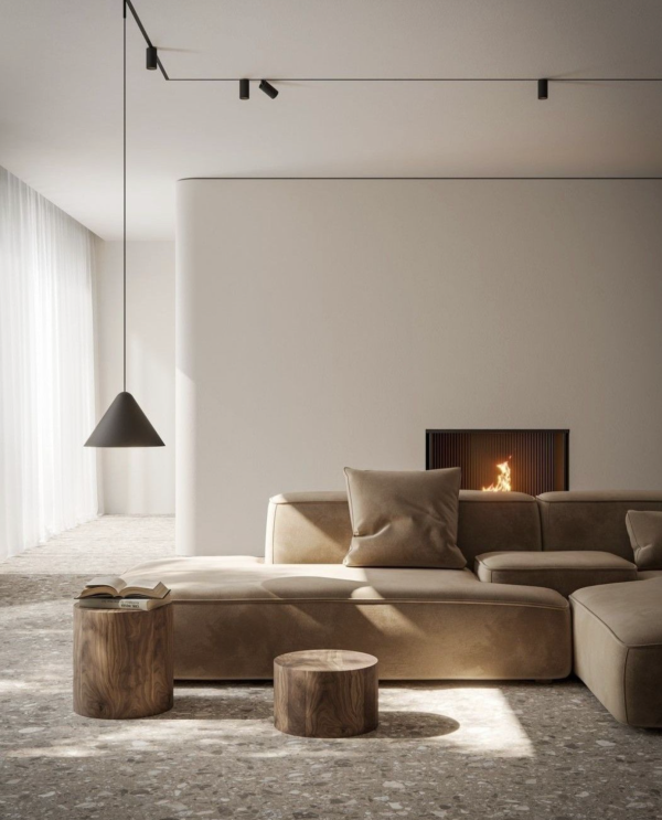 Salon minimaliste avec canapé beige, éclairé par une suspension noire, un rail de spots au plafond, la lumière naturelle d’une grande baie vitrée et la lueur d’une cheminée encastrée.