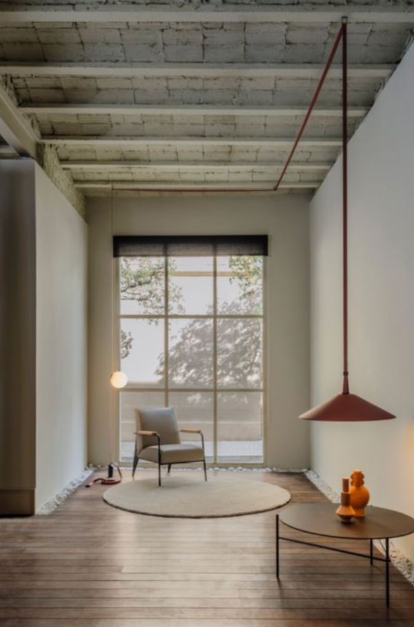 Espace minimaliste avec fauteuil et table basse, éclairé par une suspension rouge conique et une suspension boule diffusant une lumière douce près de la fenêtre.