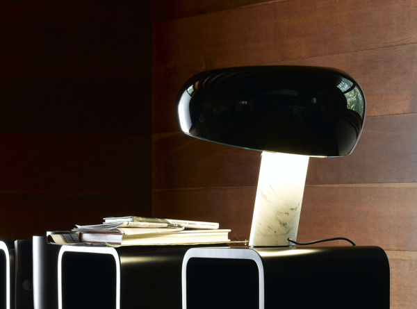 Lampe de table design avec base en marbre blanc et abat-jour noir, diffusant une lumière douce sur un meuble moderne avec livres empilés.