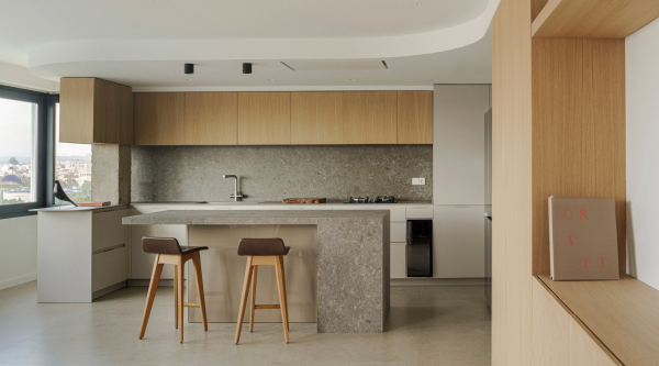 Spots encastrés et plafonniers discrets illuminant une cuisine moderne avec îlot en pierre et finitions bois.