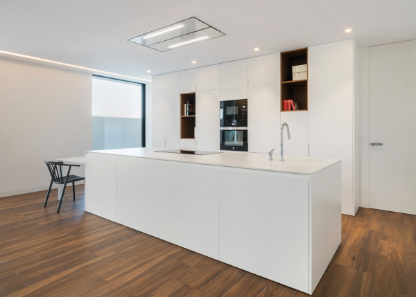 Éclairage encastré et lignes lumineuses intégrées au plafond d’une cuisine minimaliste blanche avec îlot central.