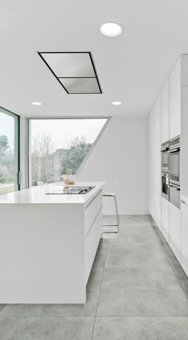 Éclairage encastré discret au plafond illuminant une cuisine minimaliste blanche avec îlot central.