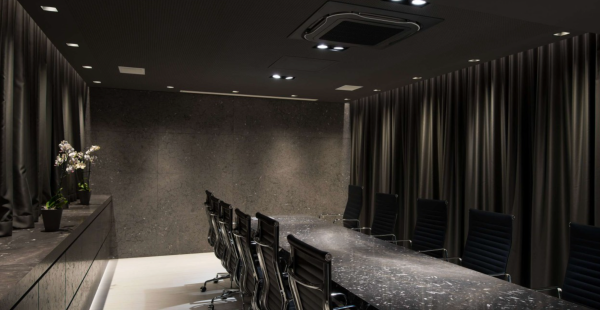 Dark and elegant meeting room with directional lighting, large stone table, and aligned black chairs.