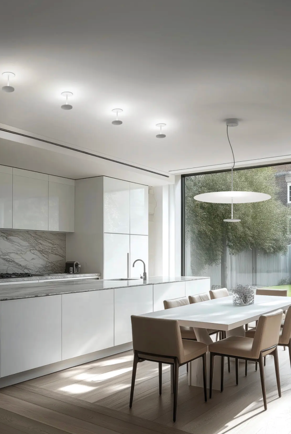 Éclairage contemporain avec plafonniers alignés et suspension circulaire au-dessus de la table dans une cuisine moderne et lumineuse.