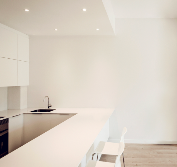 Spots encastrés au plafond éclairant une cuisine minimaliste blanche avec comptoir en angle.