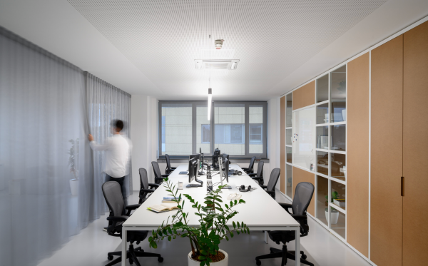 Bright contemporary office with large windows, long shared desks, and central linear lighting.