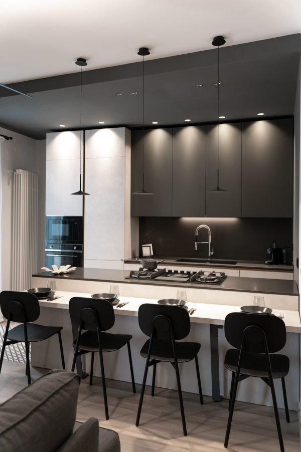 Suspensions minimalistes noires au-dessus d’un îlot de cuisine, accompagnées d’un éclairage encastré et d’un bandeau lumineux sous les meubles hauts.