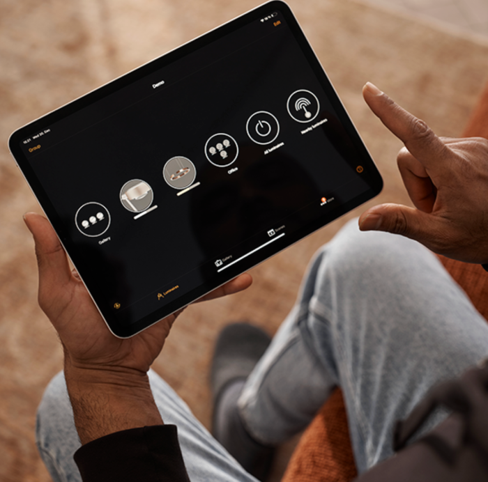 A person holding a tablet displaying the Casambi app, used to control wireless lighting with icons for different rooms and functions