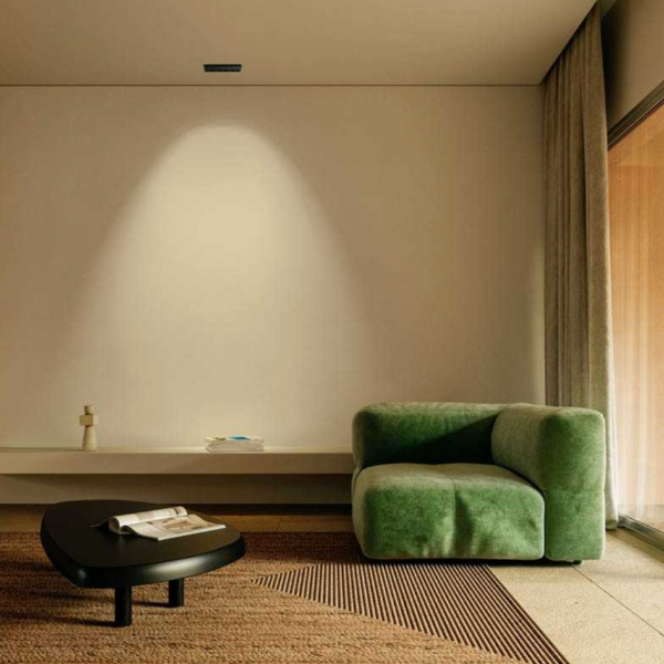 Salon minimaliste avec fauteuil vert, table basse noire et éclairage encastré au plafond projetant un faisceau lumineux sur le mur.