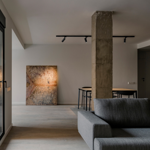Salon moderne avec projecteurs noirs montés sur rail au plafond, offrant un éclairage directionnel mettant en valeur une œuvre d’art appuyée contre le mur.