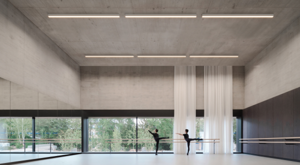 Studio de danse contemporain éclairé par des luminaires linéaires au plafond, avec deux danseurs pratiquant devant un miroir.