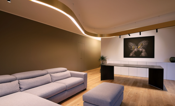 Espace de vie moderne avec luminaire courbé au plafond offrant un éclairage doux et diffus au-dessus d’un canapé et d’un espace bureau.