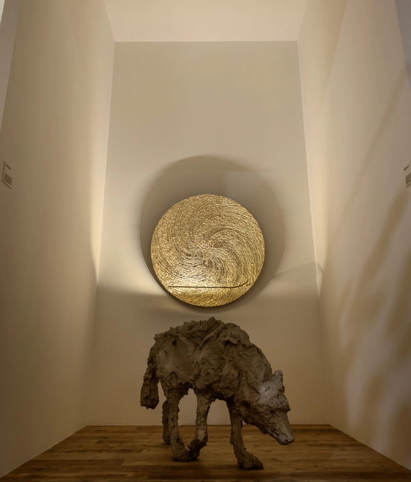 Applique murale circulaire dorée diffusant une lumière chaleureuse, accompagnée d’une sculpture de loup au premier plan.