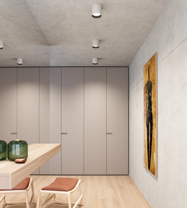 Intérieur moderne éclairé par des spots cylindriques blancs au plafond, avec table en bois clair et œuvre d’art murale.