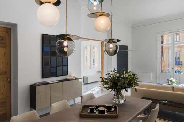 Smoked and opal blown glass pendant lights with golden metal discs, elegantly illuminating a contemporary dining room with a stone table and fresh flower arrangement.