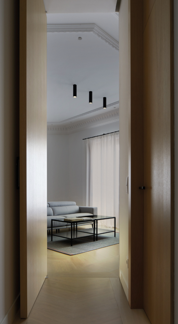 Salon élégant avec trois projecteurs cylindriques noirs en surface au plafond, diffusant un éclairage ciblé au-dessus d’un canapé gris et d’une table basse minimaliste.