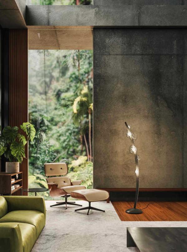 Sculptural black metal floor lamp adorned with clear glass spheres along a curved stem, casting a soft glow against a textured wall in a living room open to nature.