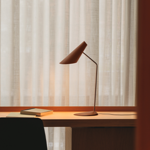 Elegant brown metal desk lamp with an adjustable conical shade and slender base, placed on a wooden desk in front of a sheer curtain.