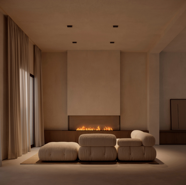Salon minimaliste éclairé par des spots encastrés au plafond, avec un canapé beige face à une cheminée moderne.