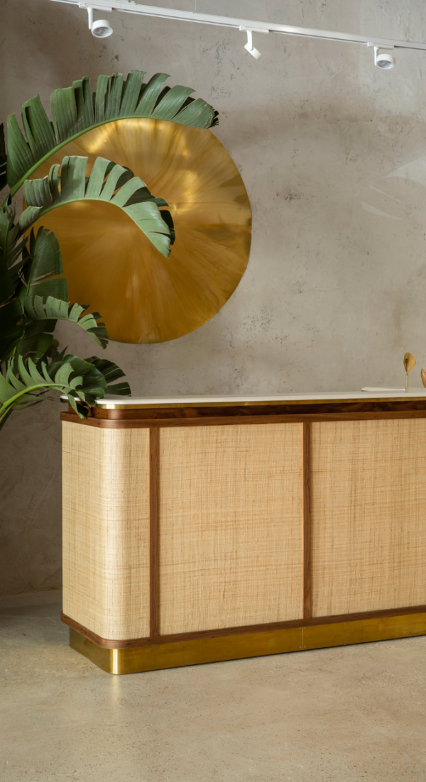 Comptoir en bois et laiton au design raffiné, éclairé par des projecteurs sur rail blancs fixés au plafond, mettant en valeur la décoration murale dorée et les plantes.