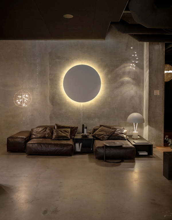 Circular wall light casting a soft halo glow above a leather sofa in an industrial-style living room.
