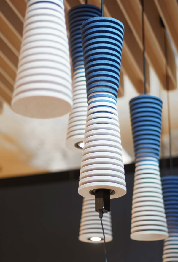 Close-up of conical acoustic pendant lights made of stacked blue and white rings, hanging beneath a slatted wooden ceiling.