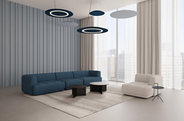 Circular acoustic pendant lights, some featuring integrated ring lighting, installed above a modern lounge area with a large blue sofa, a white armchair, and coffee tables.