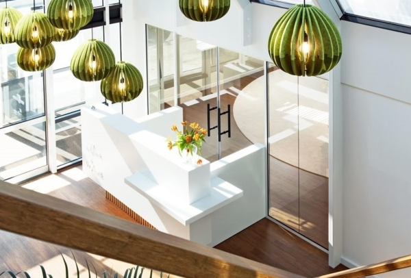Green drop-shaped acoustic pendant lights made of vertical slats with illuminated centers, installed in a bright lobby with large glass surfaces and a white reception desk.