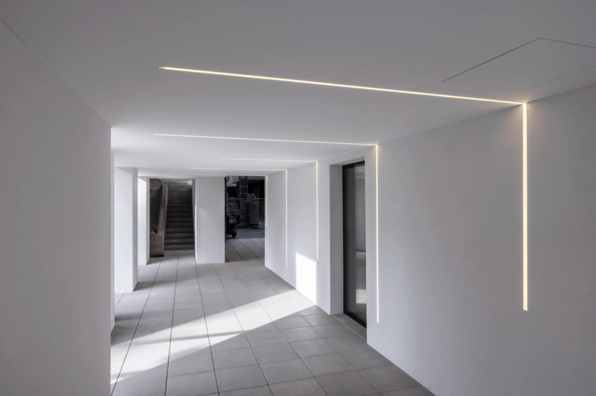 Espace architectural moderne avec des profilés linéaires LED intégrés au plafond et aux murs, créant un éclairage continu et minimaliste.